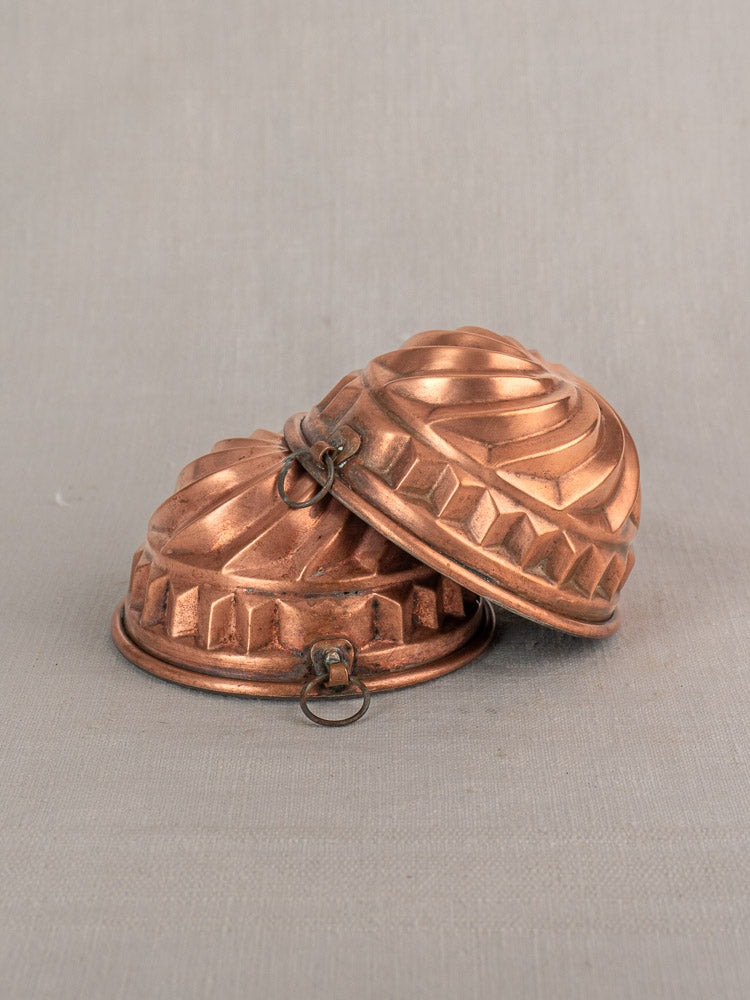 Pair of antique French copper dessert molds with spiral relief, tin-lined, stacked on neutral fabric.