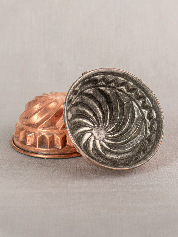 Pair of antique French copper dessert molds, one with spiral interior, one with fluted design, on neutral fabric.