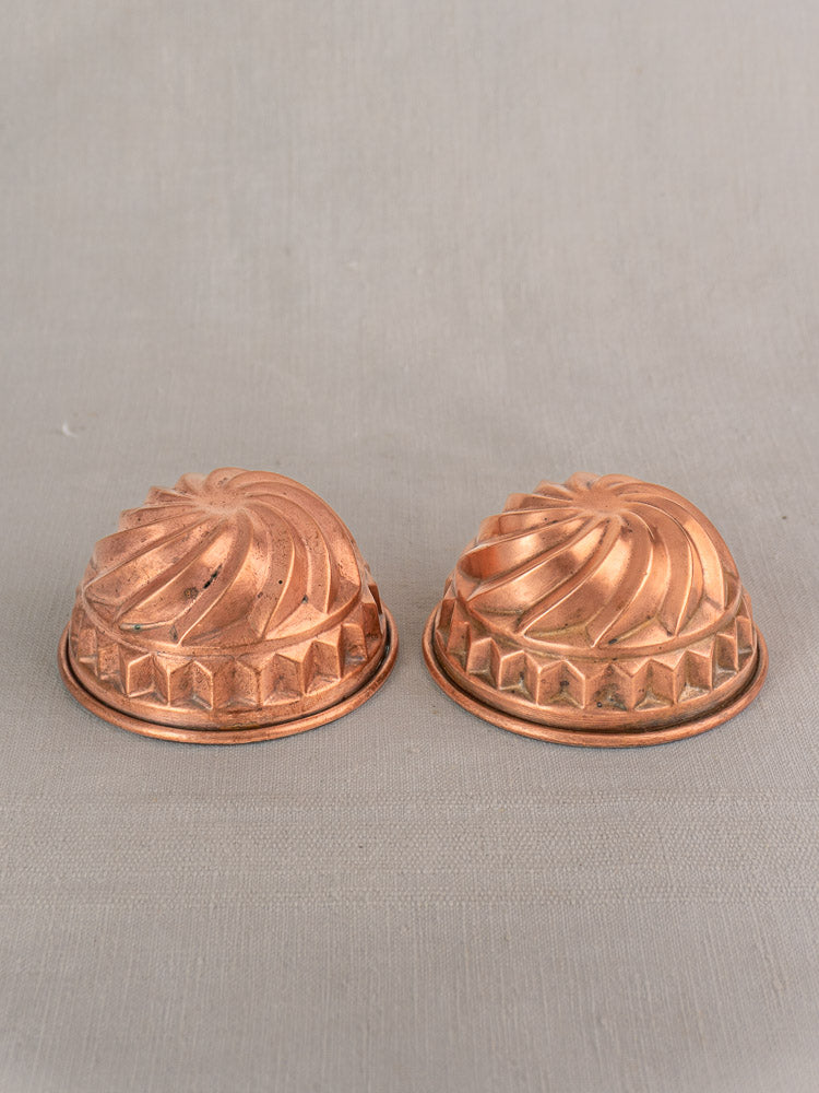 Pair of antique French copper dessert molds with spiral relief on a neutral gray fabric background.