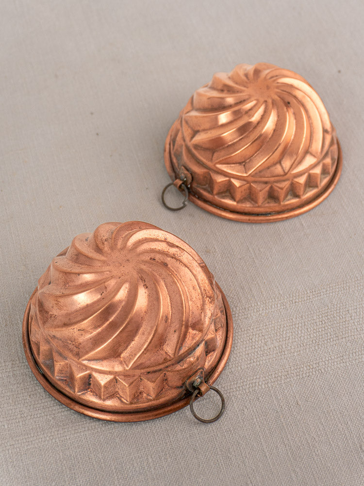 Pair of 19th-century French copper dessert molds with spiral relief, tin lining, and hanging rings on light surface.