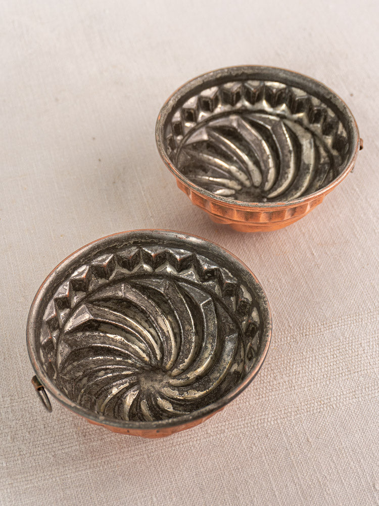 Pair of antique French copper dessert molds with spiral relief on light textured surface, 19th-century kitchenware elegance.