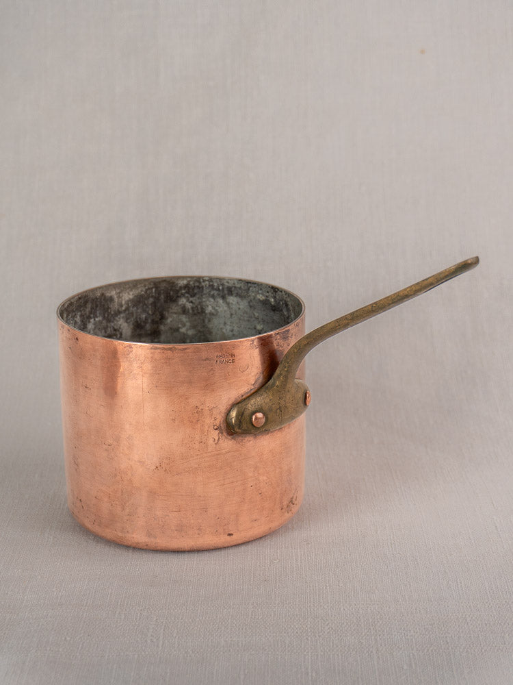 Antique French copper bain marie with Apilco porcelain insert and brass handle on light grey fabric surface.