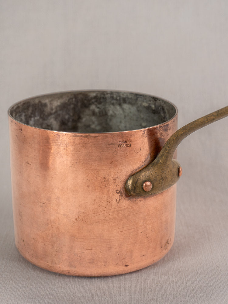Antique French copper bain marie with brass handle and Apilco porcelain insert, stamped "Made in France," on light gray surface.
