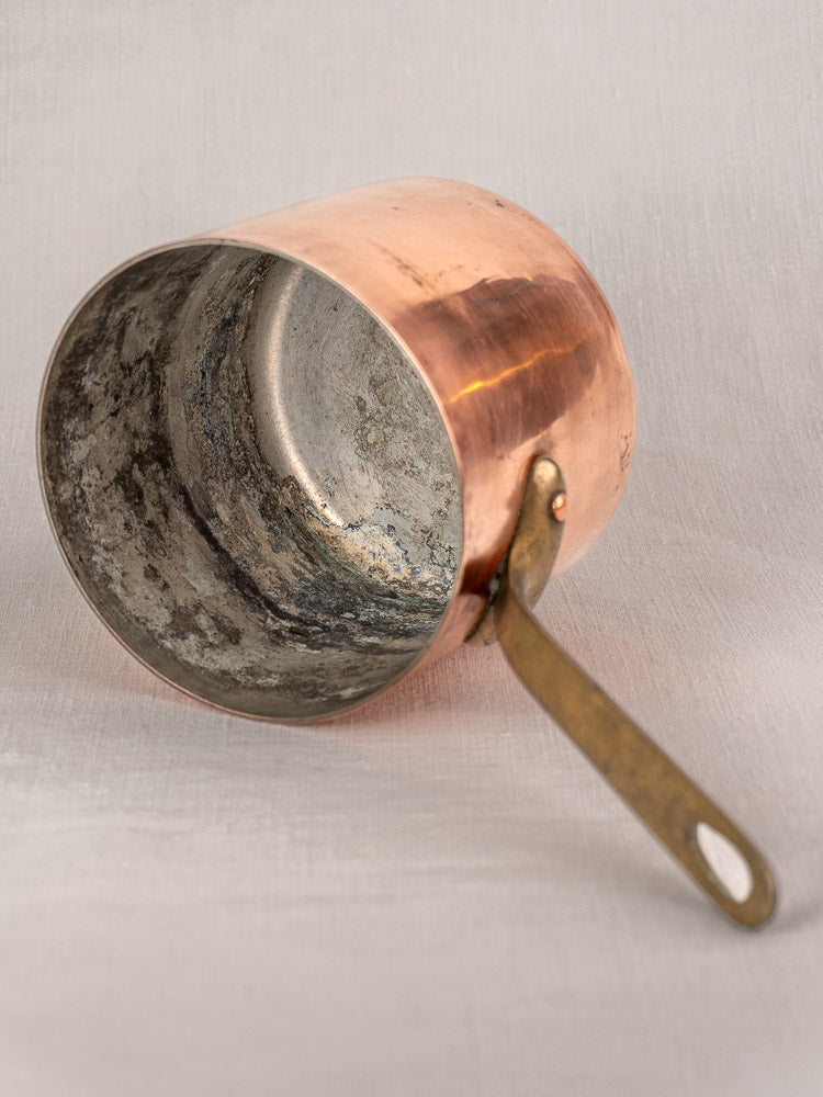 Mid-century French copper bain marie with brass handle and Apilco porcelain insert on light fabric background.