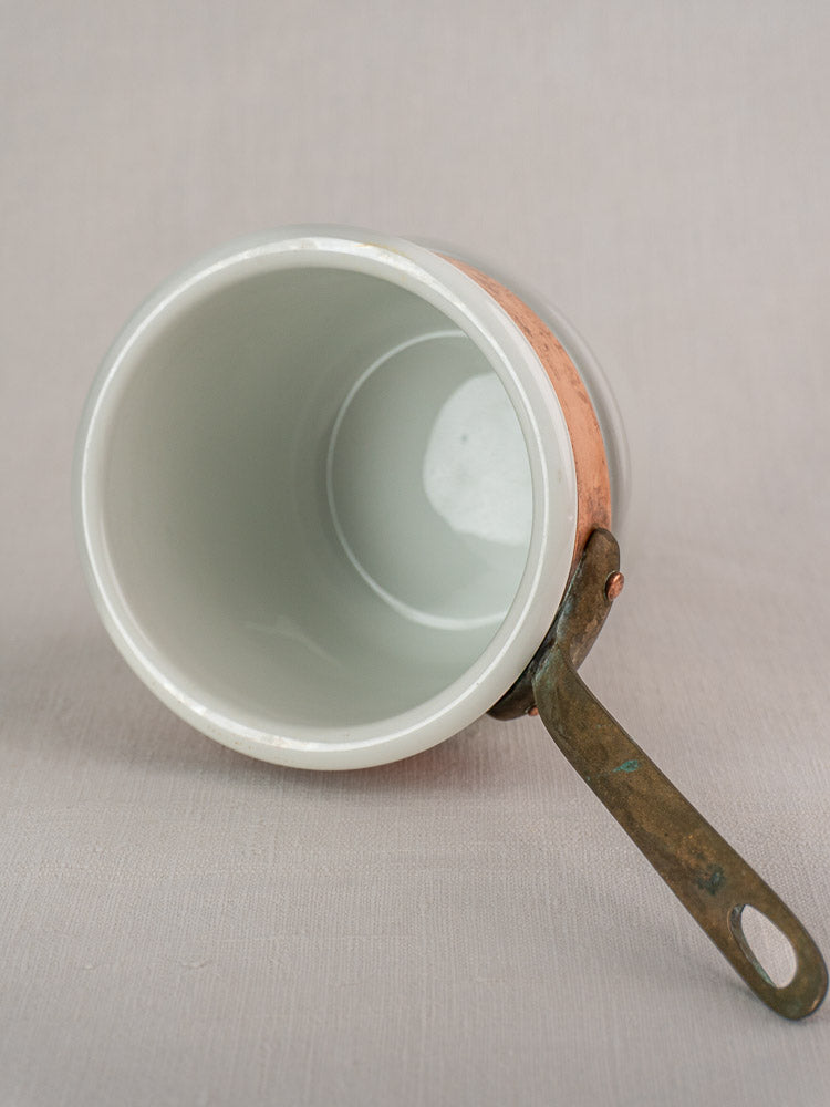 Antique French copper bain marie with Apilco porcelain insert, metal handle, and white ceramic interior on light fabric.