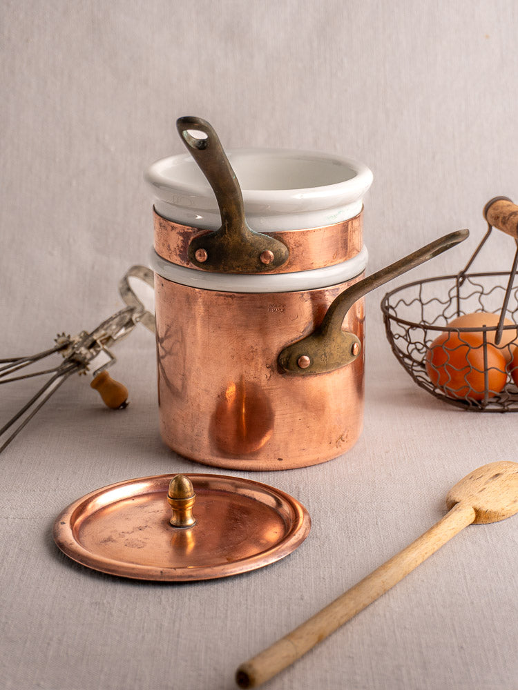 Antique French copper bain marie with Apilco porcelain insert, copper lid, spoon, beater, eggs on table.