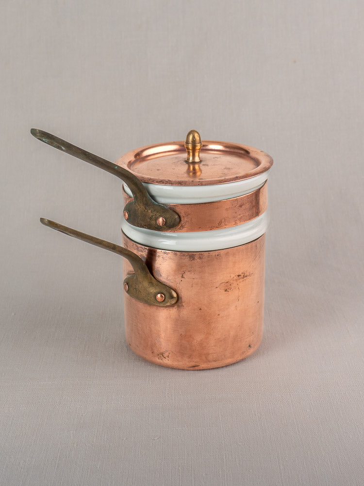 Antique French copper bain marie with Apilco porcelain insert, brass handles, and lid on a light gray surface.