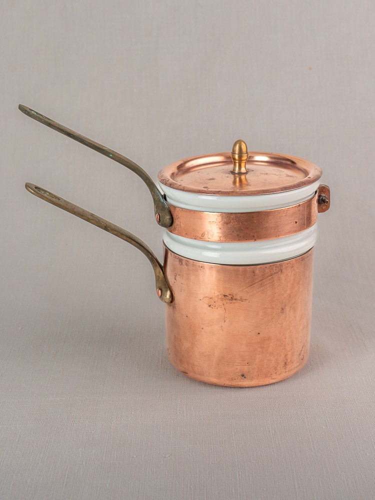 Mid 20th century French copper bain marie with Apilco porcelain insert, long handles, and brass knob on neutral background.