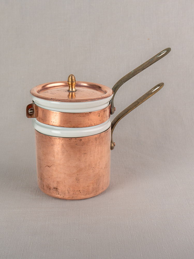 Antique French copper bain marie with Apilco porcelain insert, brass handles, and lid on a gray background.