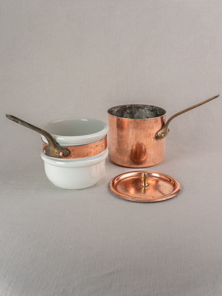 Antique French copper bain marie with brass handle and two Apilco porcelain inserts on light gray surface.