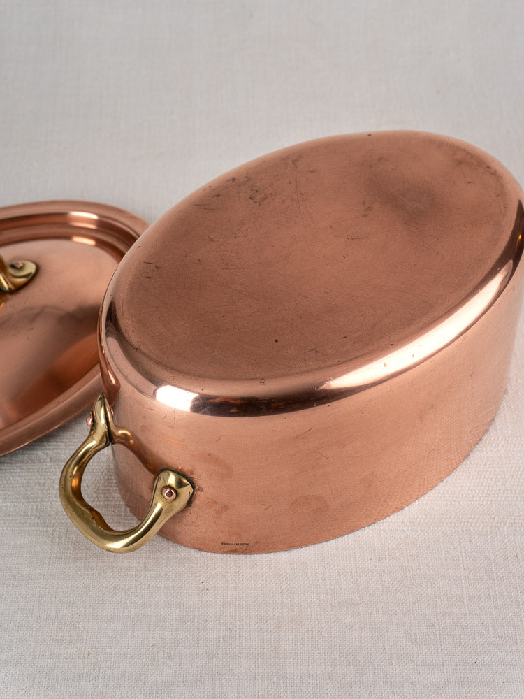 Vintage French copper cocotte with brass handles and domed lid, displayed on a pale textured surface.