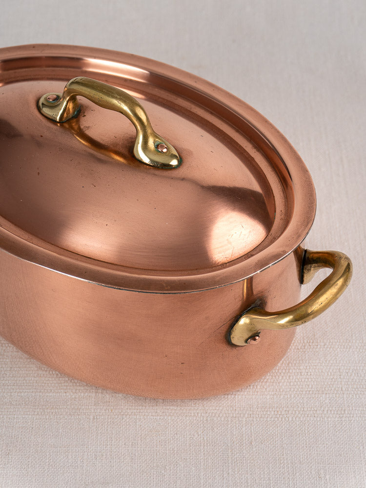 Vintage French copper cocotte with domed lid and brass handles on a light textured surface.