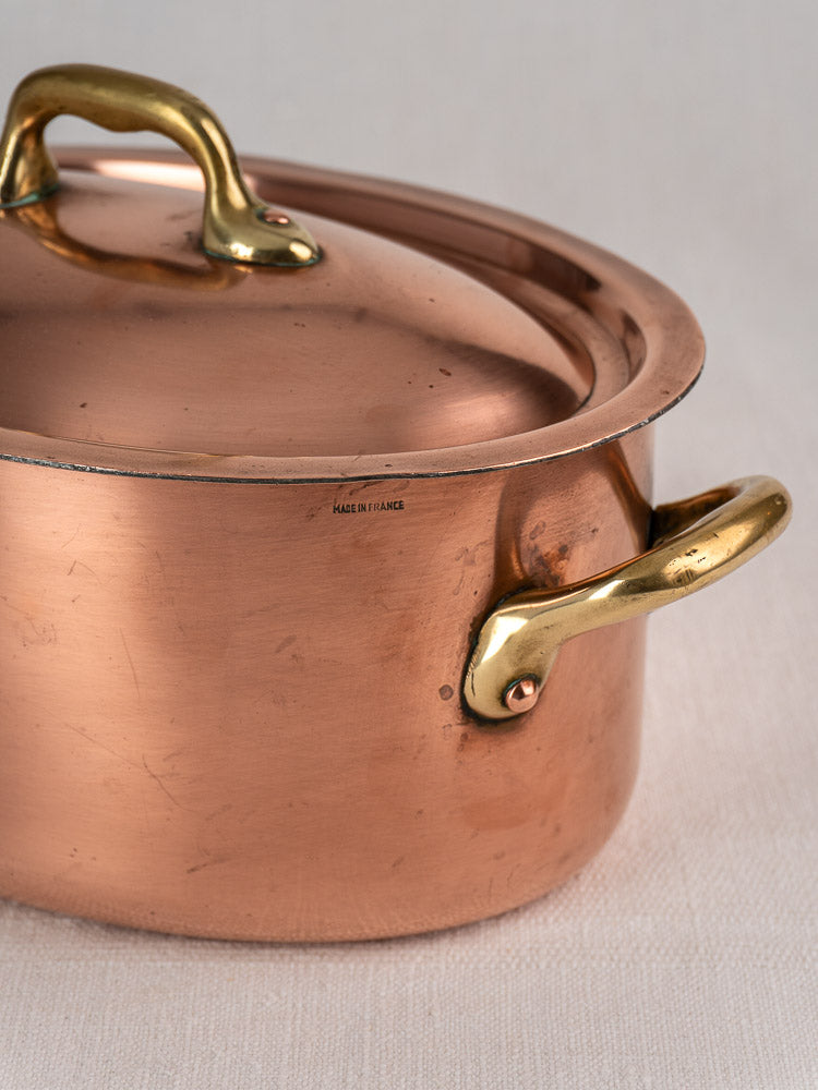 Vintage French copper cocotte with domed lid and brass handles on light fabric, marked Made in France.