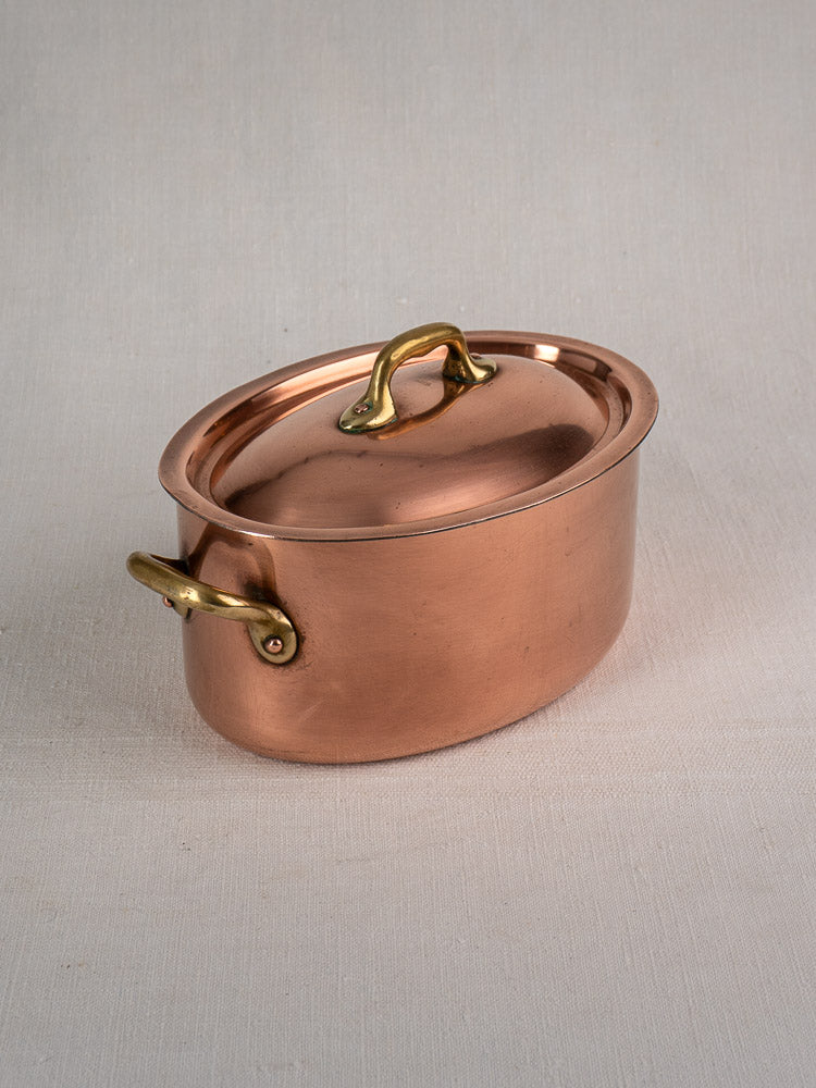 Vintage French copper cocotte with brass handles and domed lid on a light fabric surface.
