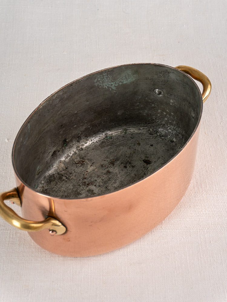 Vintage French copper cocotte with brass handles and domed lid on white fabric surface.