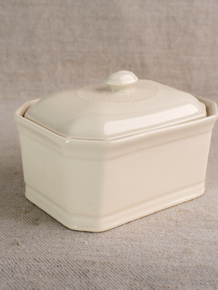 Antique French porcelain terrine with cream glaze and matching lid on neutral textured fabric, classic early 20th-century style.