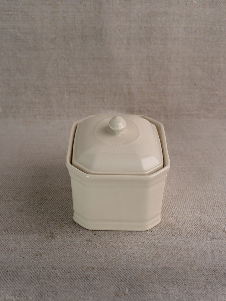 Small cream-glazed French porcelain terrine with matching lid and round knob, displayed on textured beige fabric.