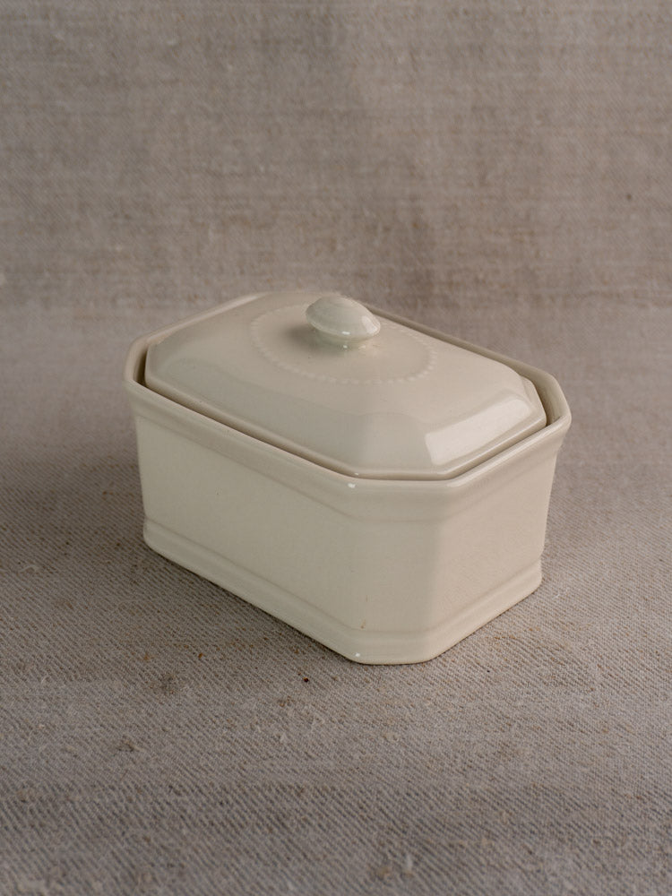Early 20th-century French porcelain terrine with cream glaze and fitted lid on textured beige fabric.