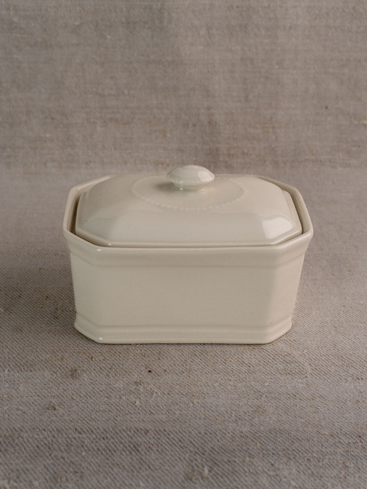 Antique French porcelain terrine, early 20th century, cream glaze, rectangular with lid and knob, on beige textured fabric.