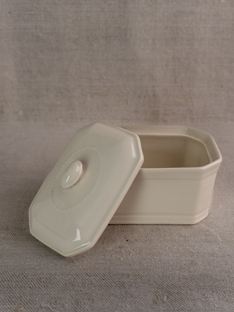 Antique French porcelain terrine with cream glaze and matching lid displayed on textured beige fabric.