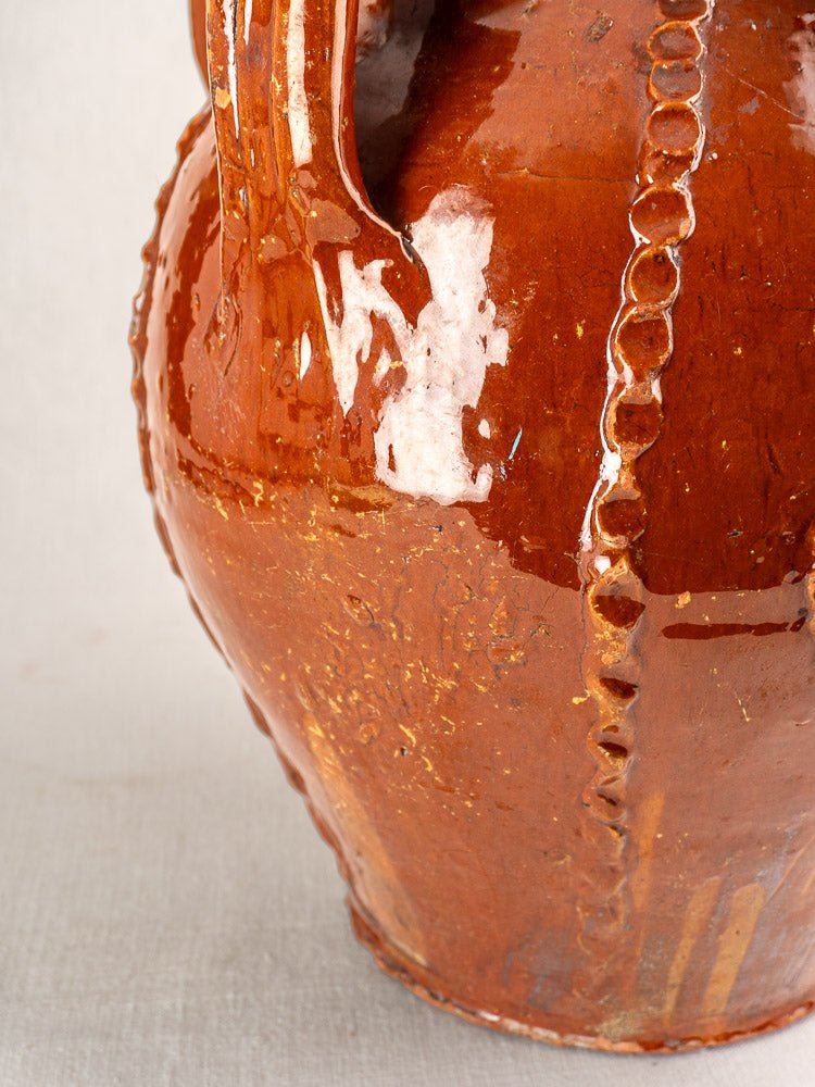 Shiny brown glazed French ceramic jug with raised wavy detailing and a sturdy handle.