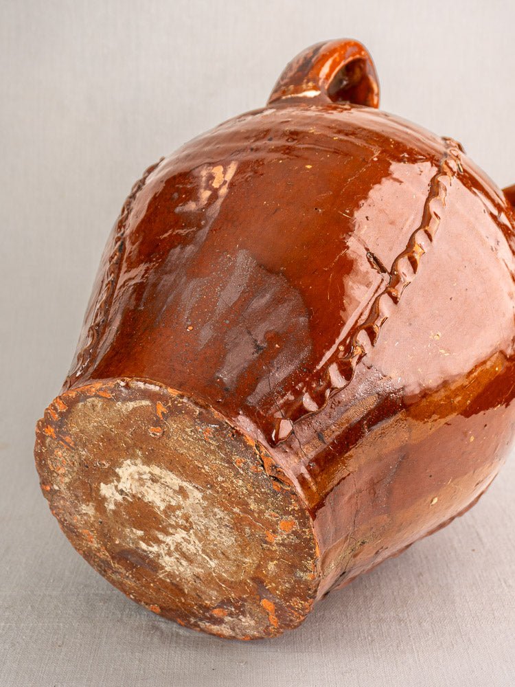 Antique French Dordogne brown glazed earthenware oil jug with stitched repairs, unglazed base on gray surface.