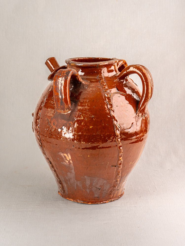 Antique French Périgord earthenware walnut oil jug with three handles and decorative raised seams.