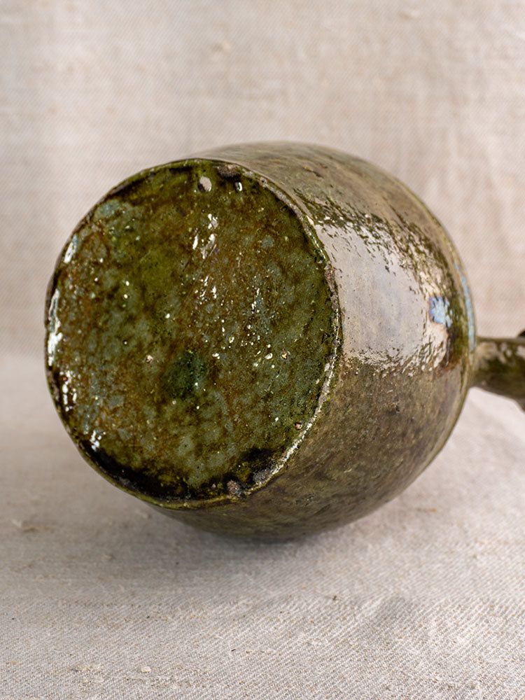 Antique French green-glazed earthenware gargoulette base, circa 1850, rustic glaze texture on neutral fabric surface.