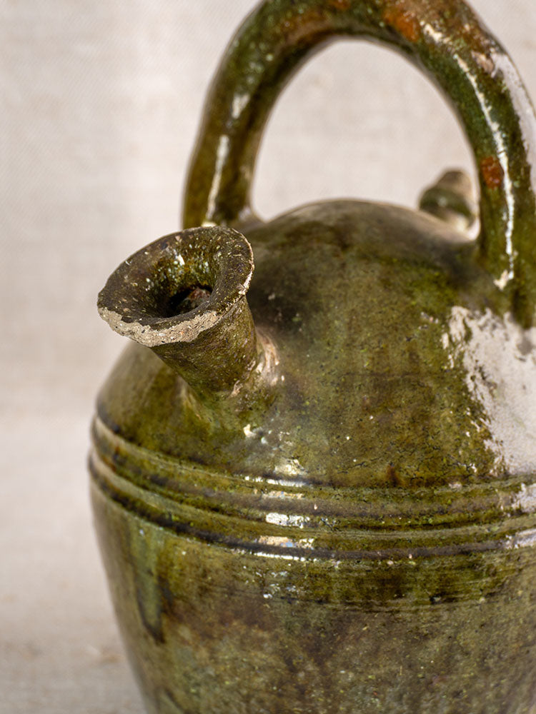 Antique French green glazed earthenware gargoulette jug, circa 1850, with handle and ridged surface on a neutral background.
