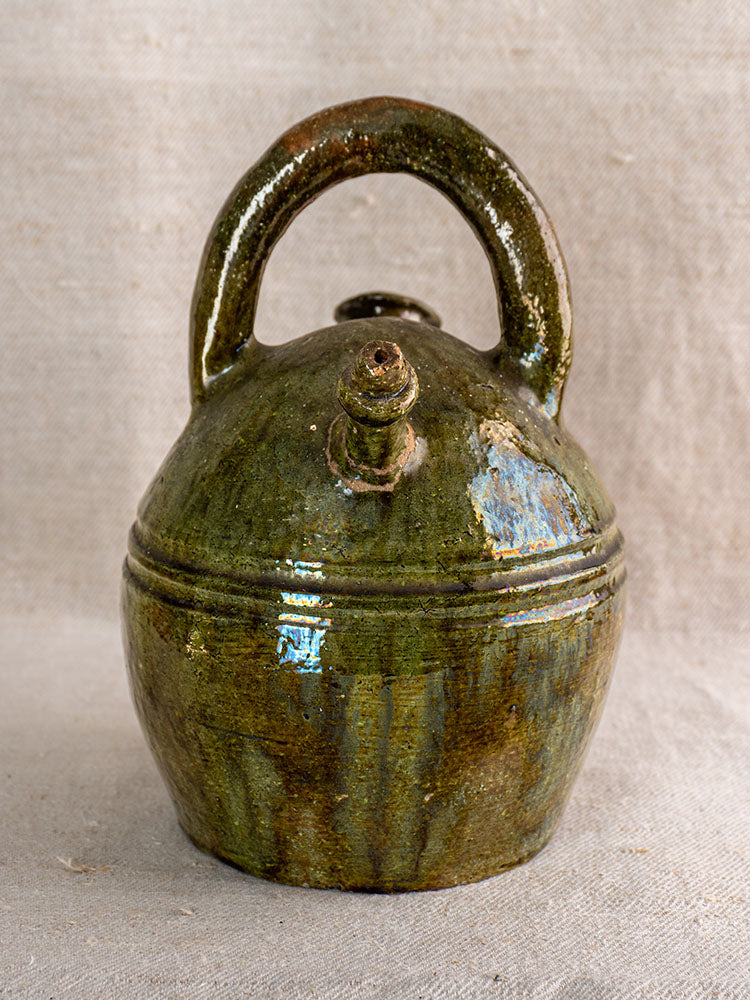 Antique French green-glazed earthenware gargoulette, circa 1850, with top handle and angled spout on neutral fabric.