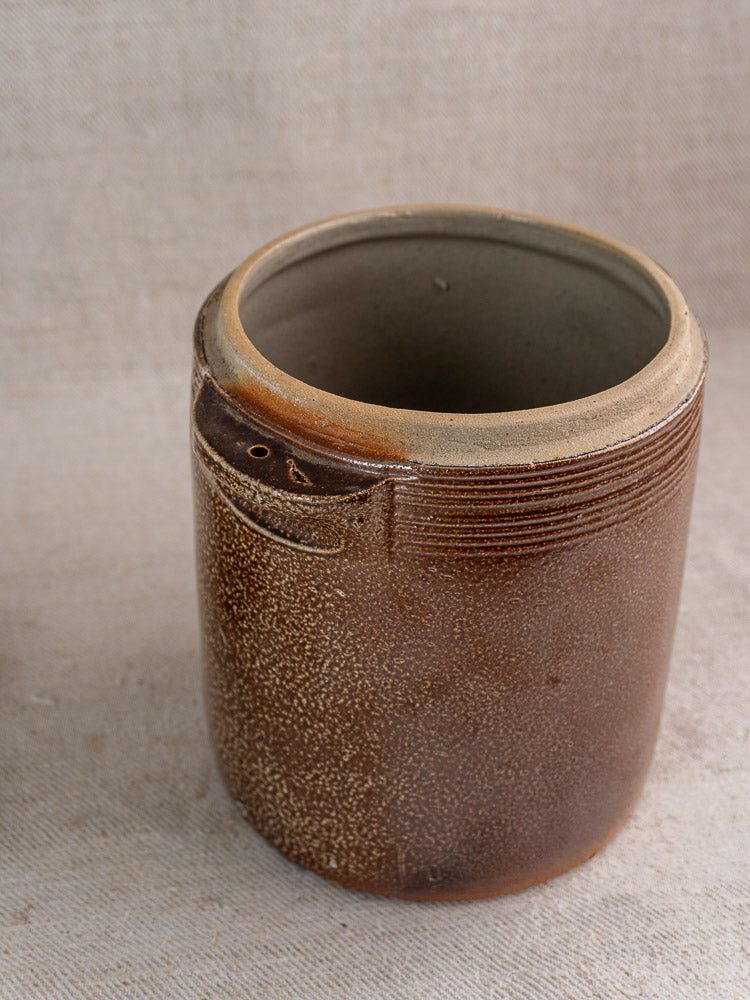 Antique French stoneware grease pot with salt glaze, matching lid, and textured brown finish on fabric backdrop.
