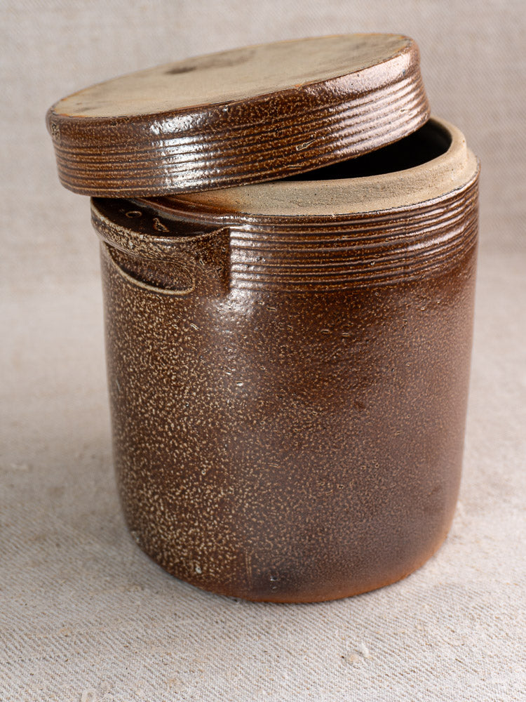 Antique French stoneware grease pot with salt glaze and lid, speckled design, on neutral surface.