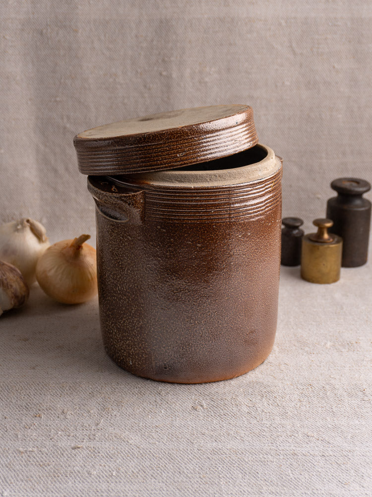 Antique French stoneware grease pot with brown salt glaze and lid, on textured cloth.