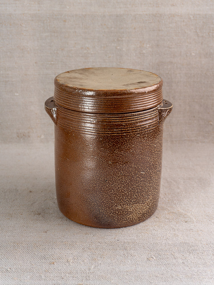 Antique French stoneware grease pot with salt glaze, matching lid, and two side handles on fabric.