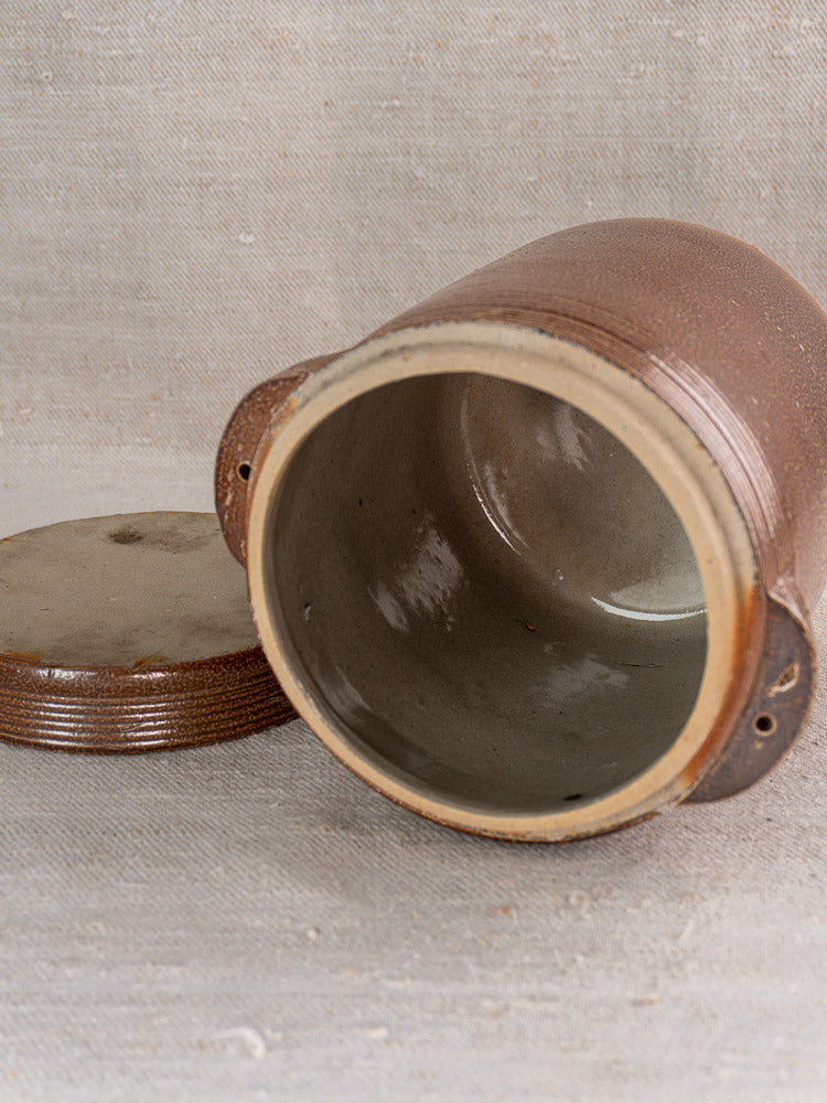 Antique French stoneware grease pot with lid off, showing salt-glazed interior on fabric background.