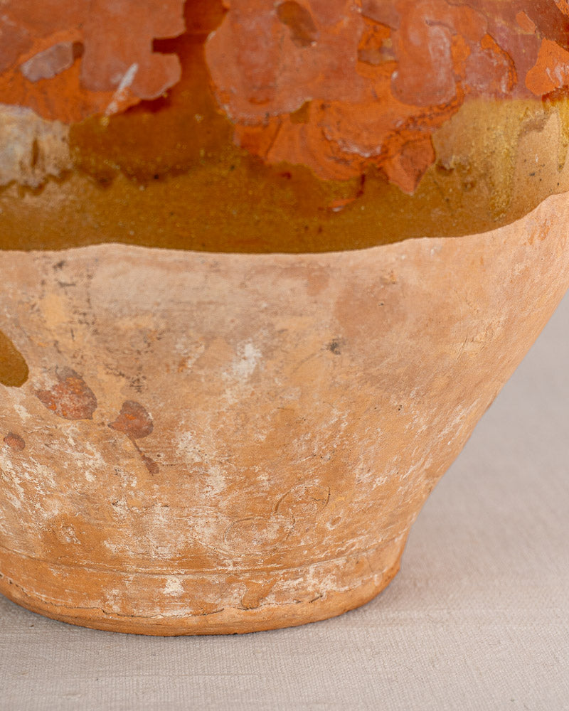 Antique French earthenware bonbonne with bichrome glaze, reddish-brown and beige tones, rustic texture on light gray fabric.