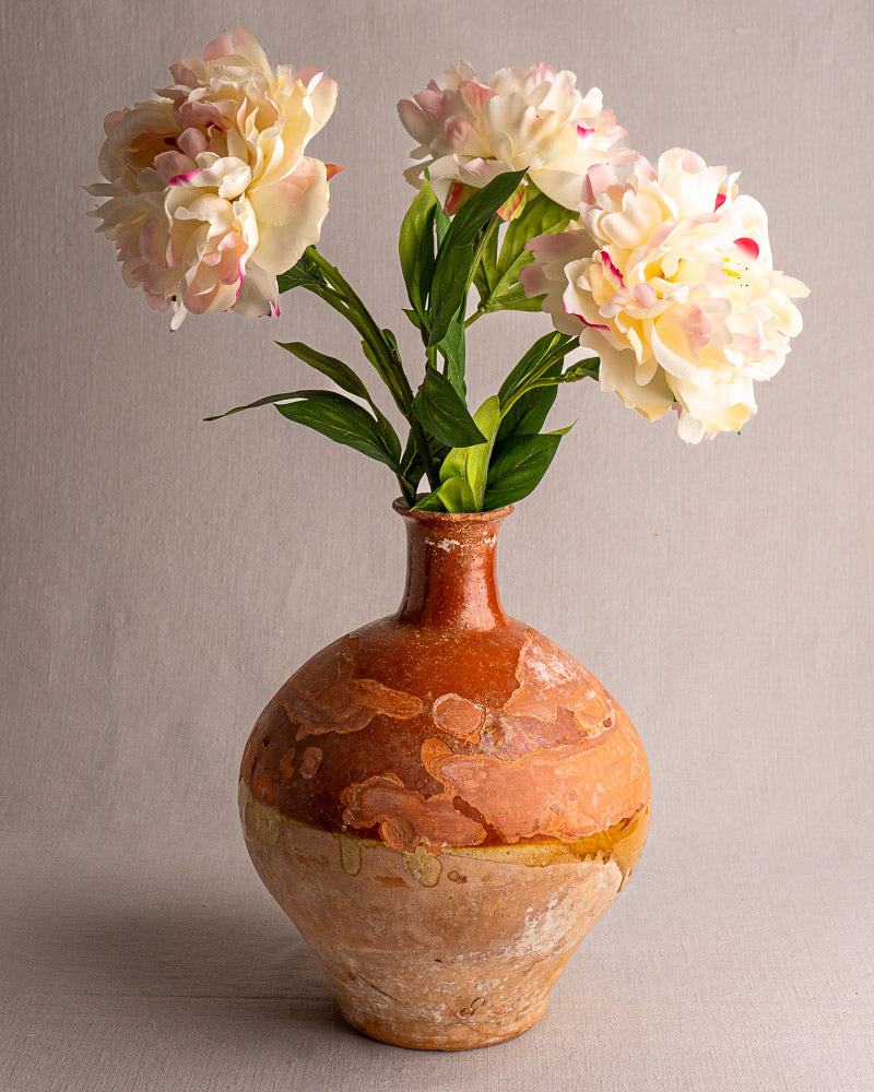 Antique French earthenware bonbonne with brown and tan glaze, holding three faux cream peonies, on a neutral backdrop.