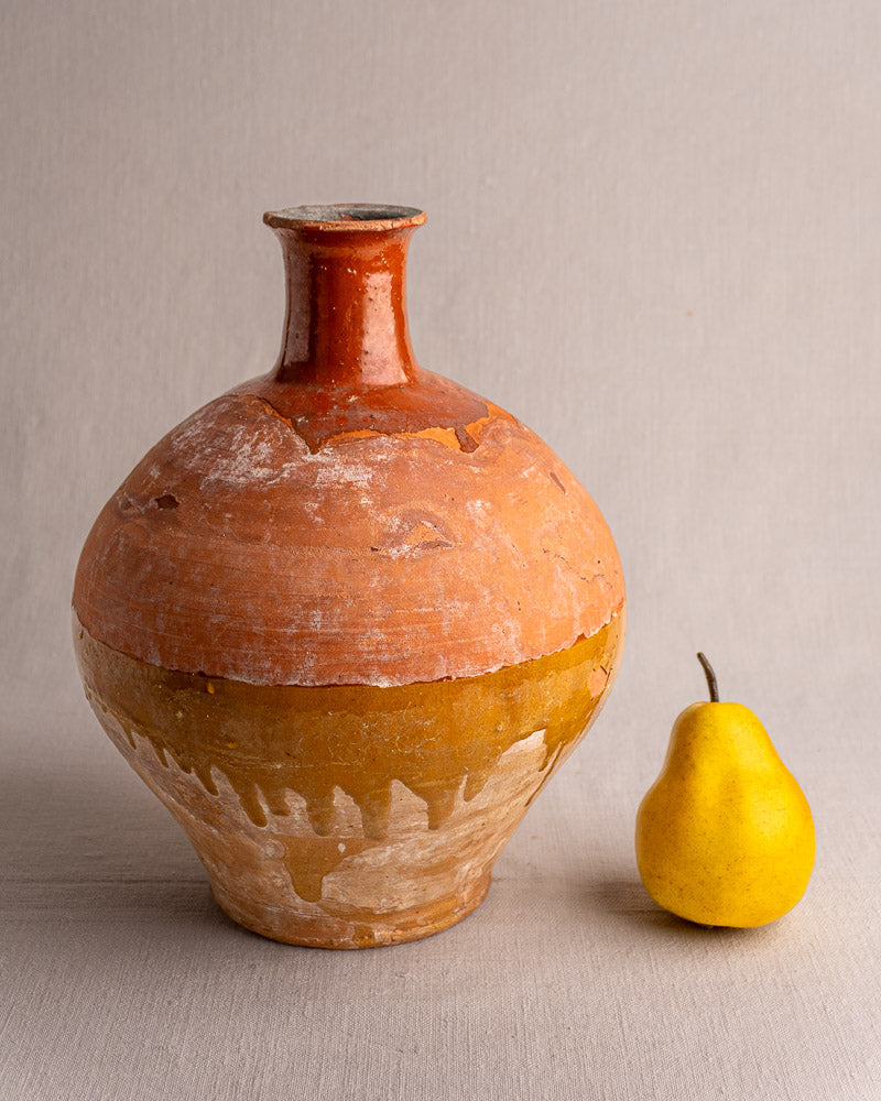Antique French earthenware hand-thrown bonbonne with bichrome glaze, displayed next to a yellow pear on a beige surface.