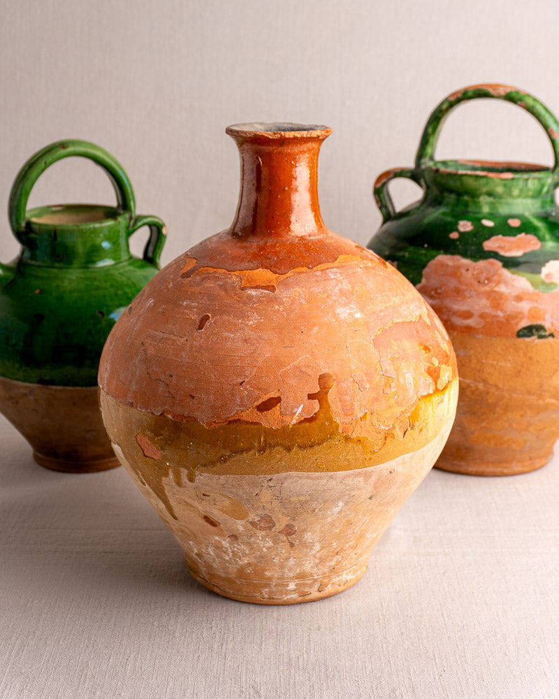 Set of three antique French earthenware bonbonnes with worn orange, yellow, and green glazes on a light surface.