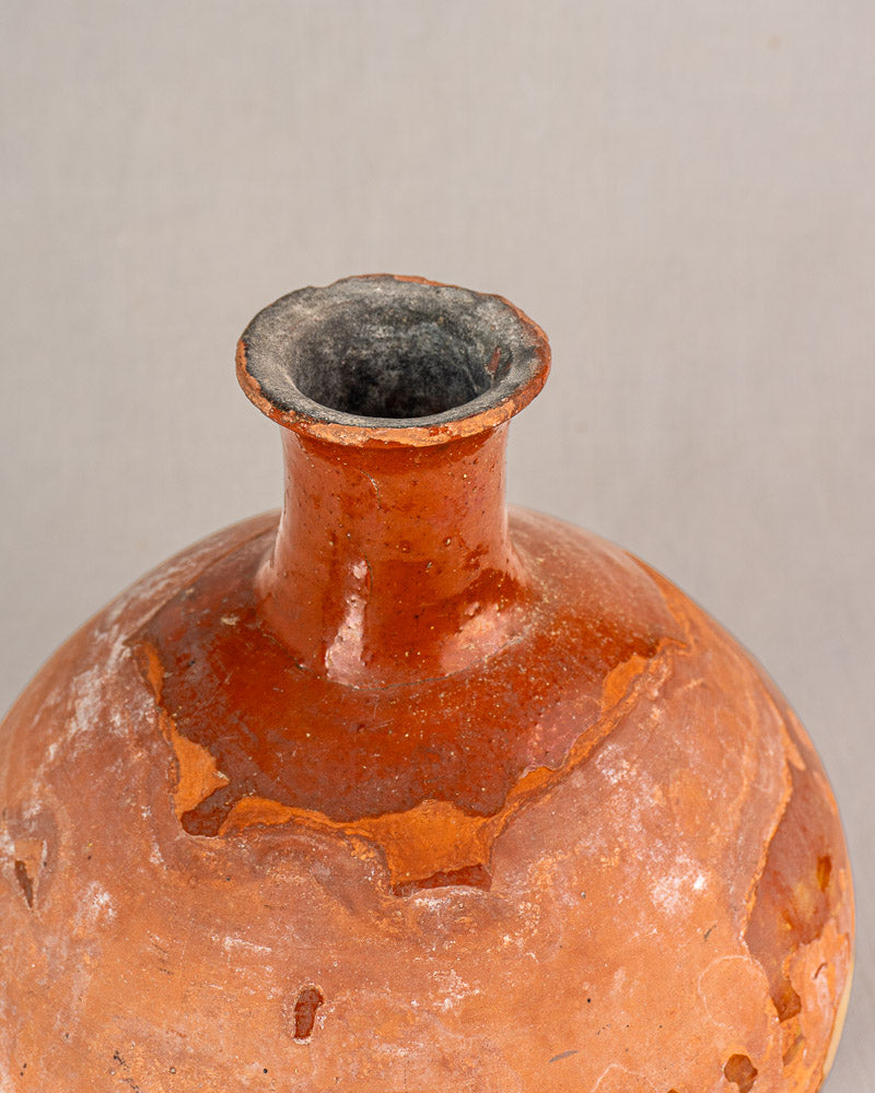 Close-up of antique French earthenware bonbonne bottle with bichrome glaze and weathered surface, plain light background.