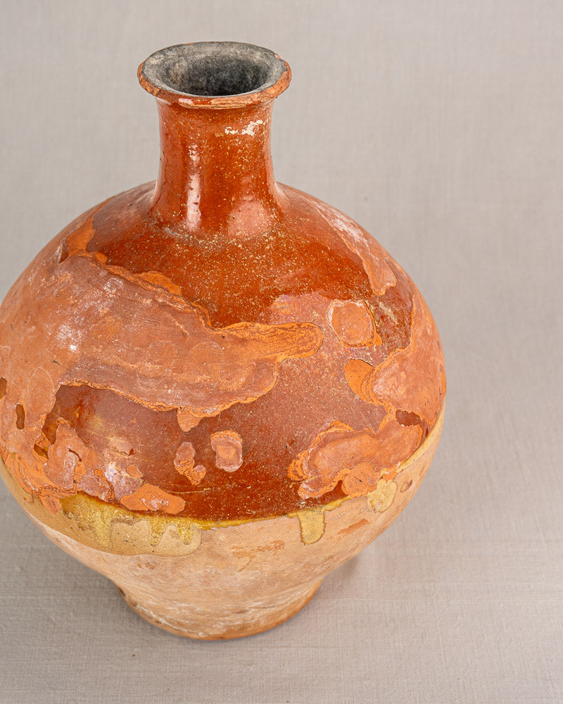 Antique French earthenware bonbonne with round reddish-brown body, narrow neck, faded glaze, worn surface, on light gray background.