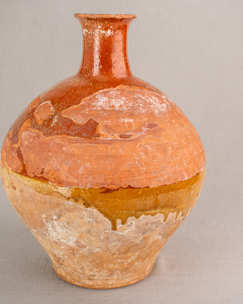 Antique French earthenware bonbonne with bichrome glaze, narrow neck, textured surface, and rustic brown-orange tones.