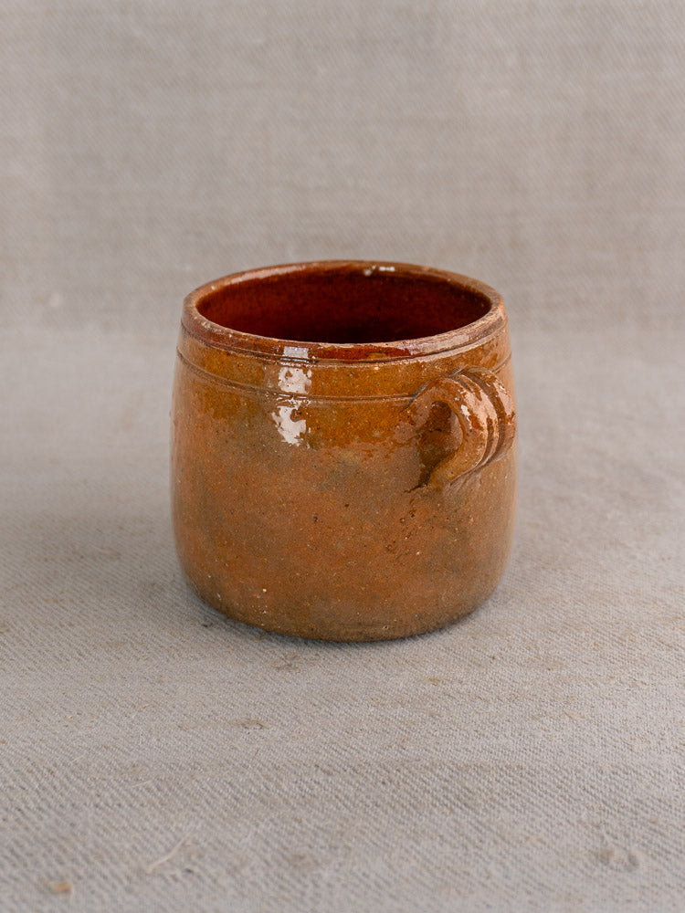 Small round antique French Vallauris terracotta pot with rich brown glaze and simple handle on gray fabric.