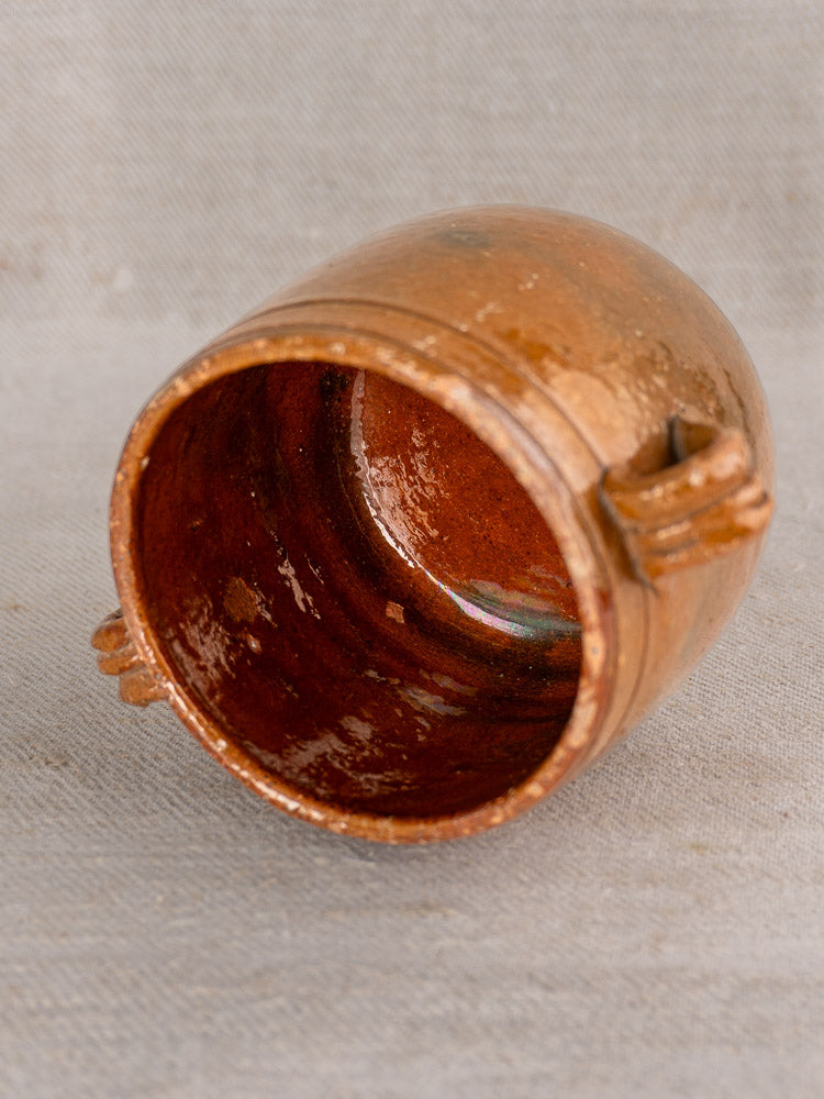 Small round Vallauris glazed terracotta cup with side handles, shown on a textured gray surface.