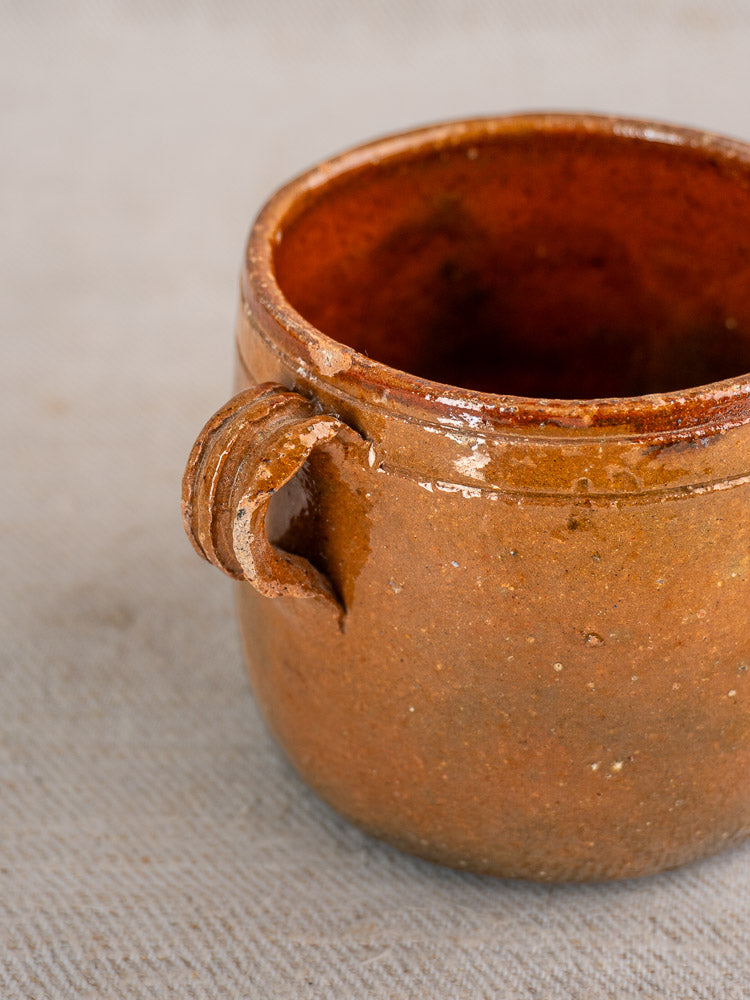 Antique French Vallauris pot with rustic brown ceramic finish and handmade handle on light textured surface.
