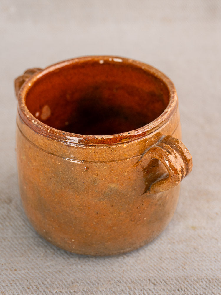 Rustic brown ceramic Vallauris pot with two handles, shown from above on gray textured surface.