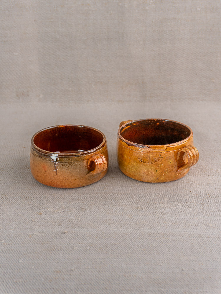 Three antique French Vallauris glazed terracotta pots with textured handles on a neutral fabric surface.