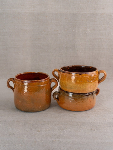 Three glazed terracotta Vallauris mugs with brown hues and subtle glaze variations on gray surface.
