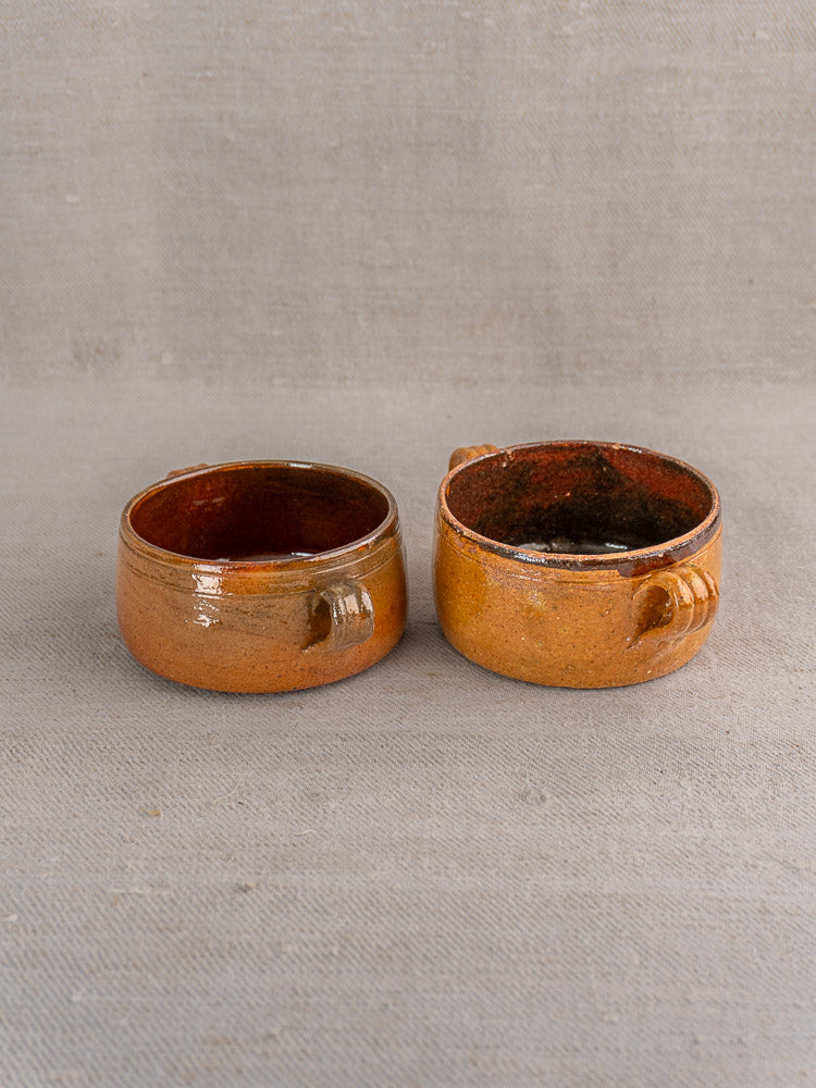Three petite, round brown-glazed antique French Vallauris terracotta pots on textured light gray fabric.