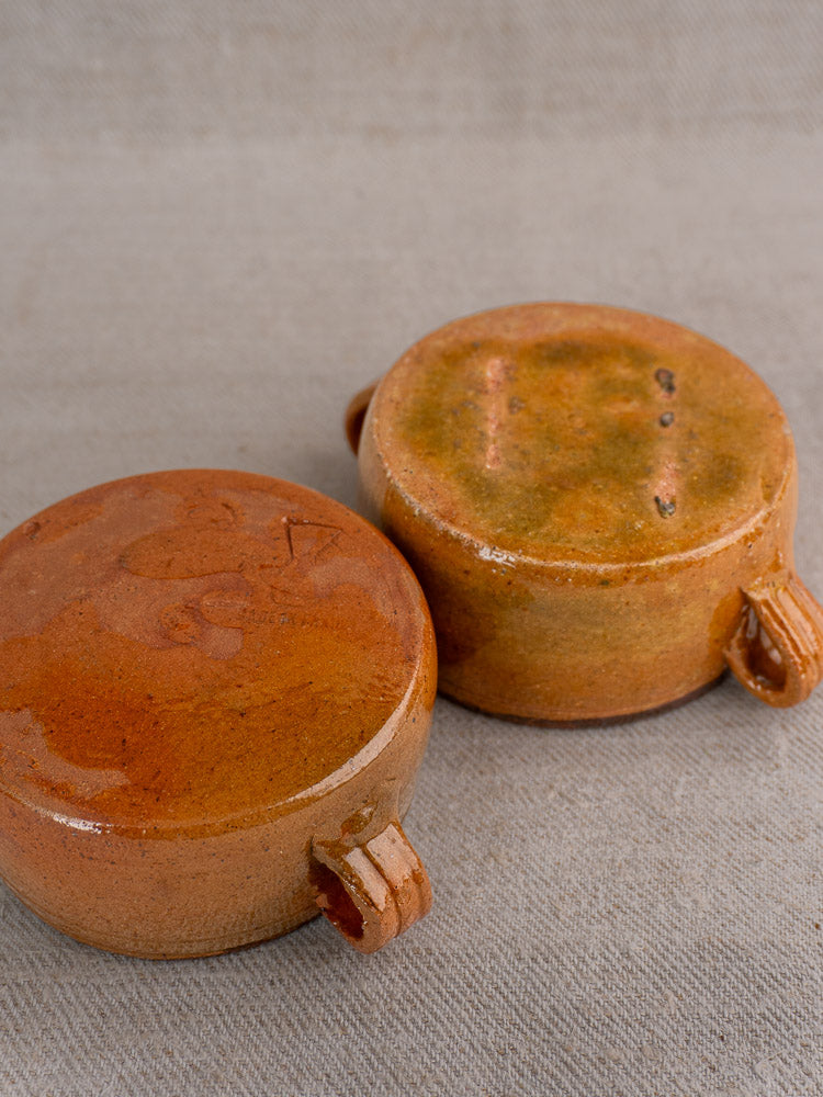 Three brown glazed terracotta French Vallauris bowls upside down on a light beige fabric surface.